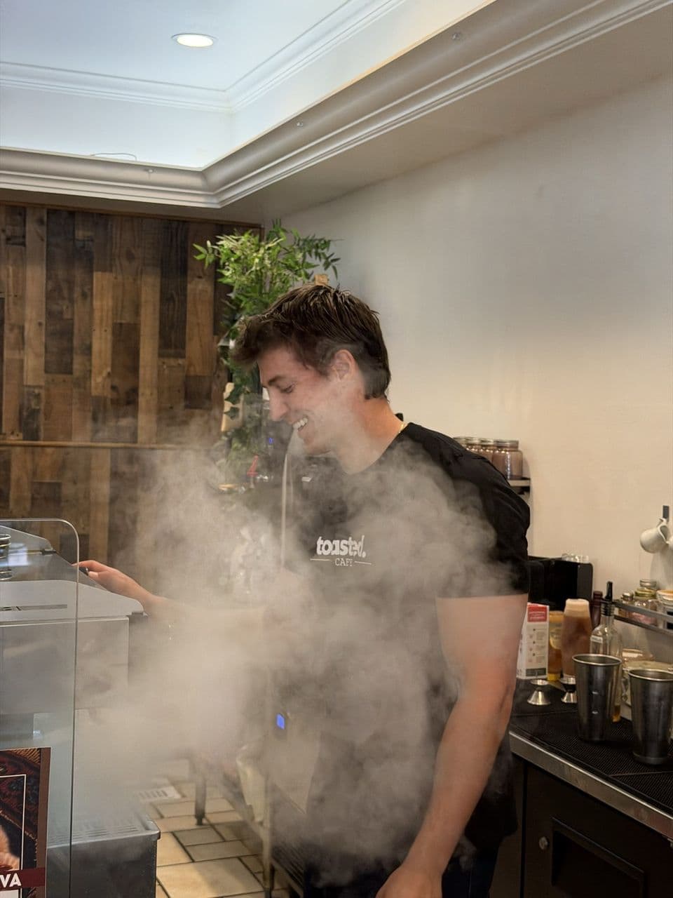 Barista in a Toasted Cafe shirt pulling a shot of espresso behind a cloud of steam