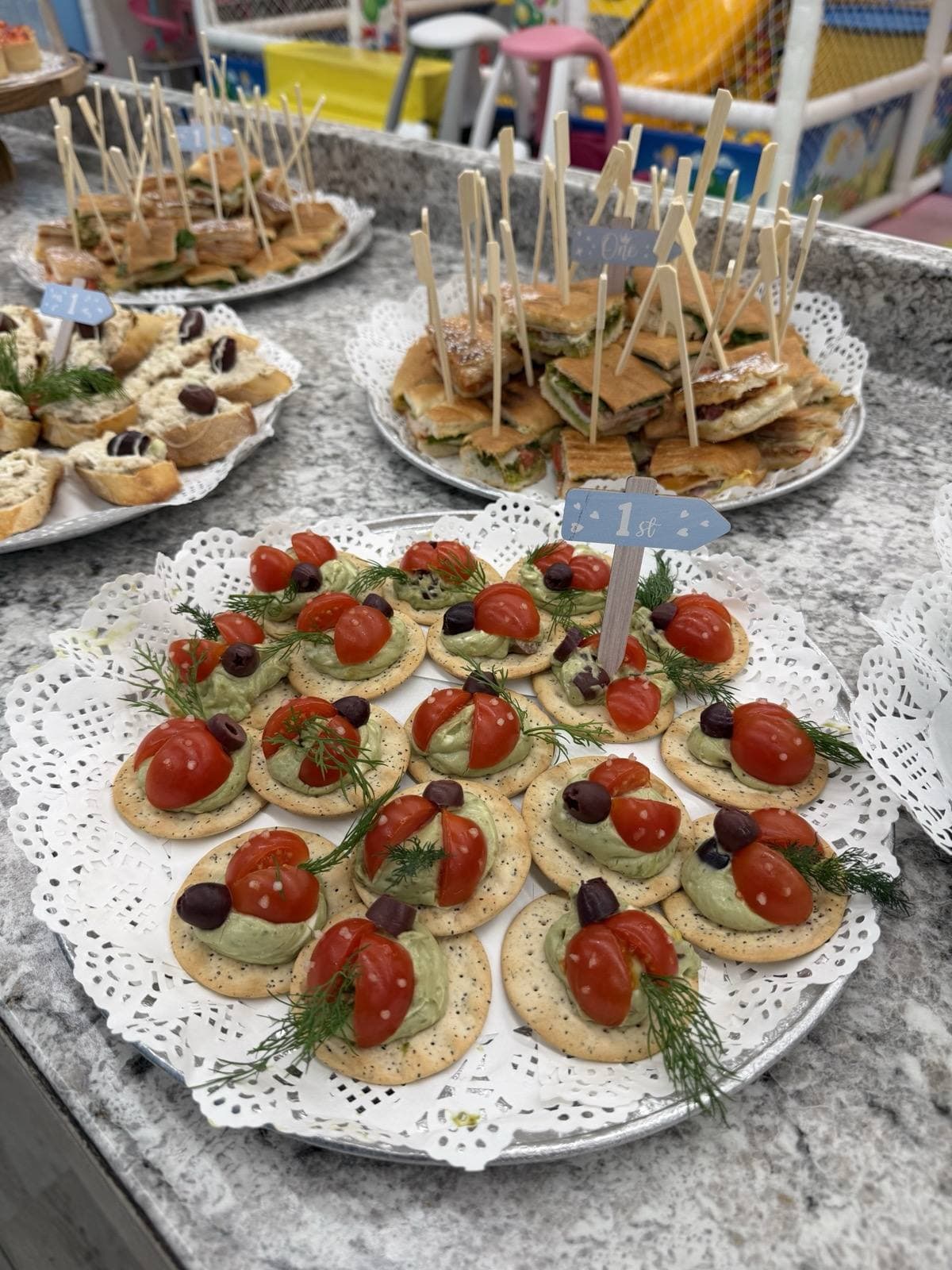 Round crackers topped with avocado spread, cherry tomato, olive and dill