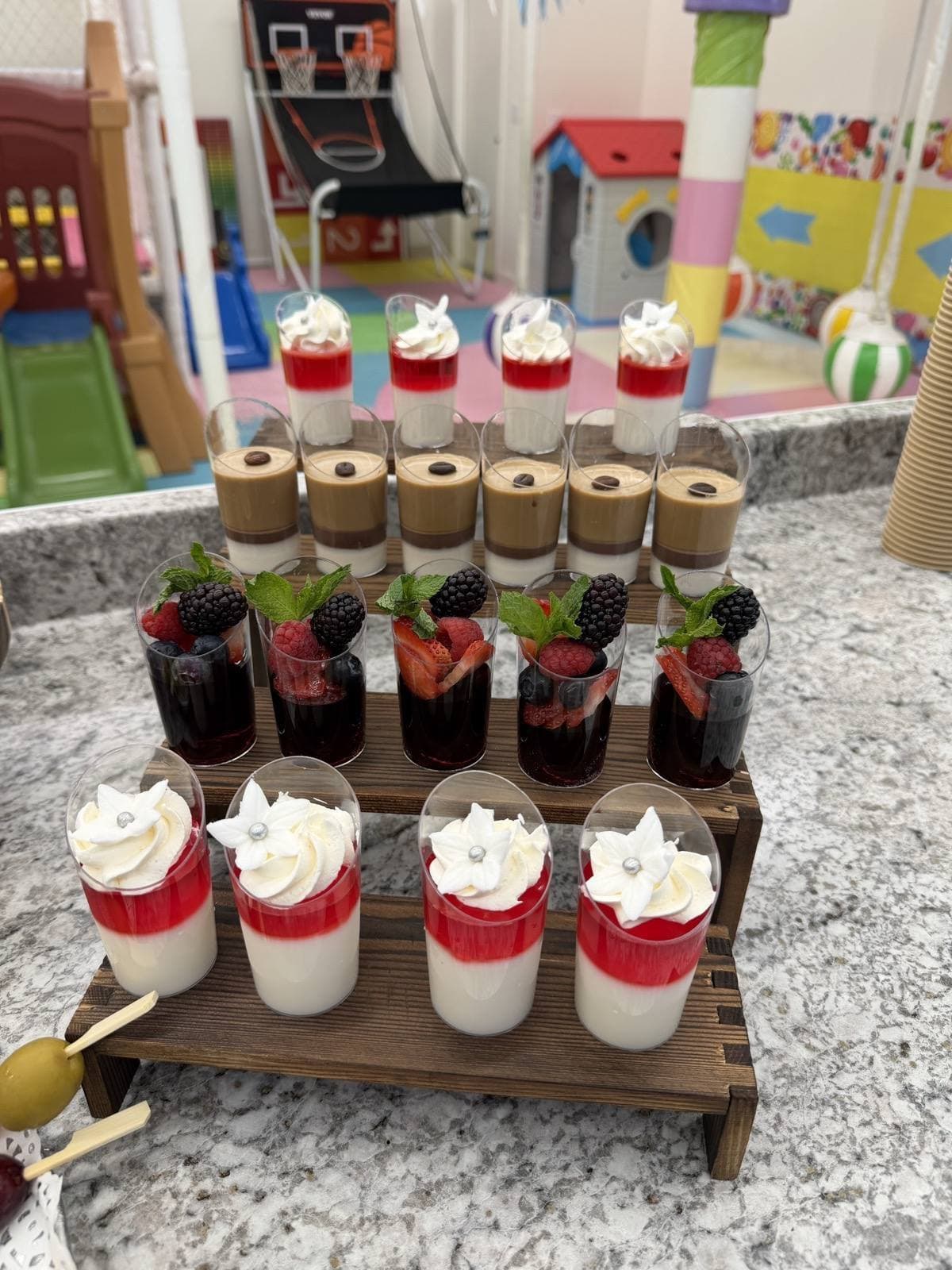 Tiered dessert display — layered cream cups, berry cups with mint, and coffee dessert cups on a wooden riser